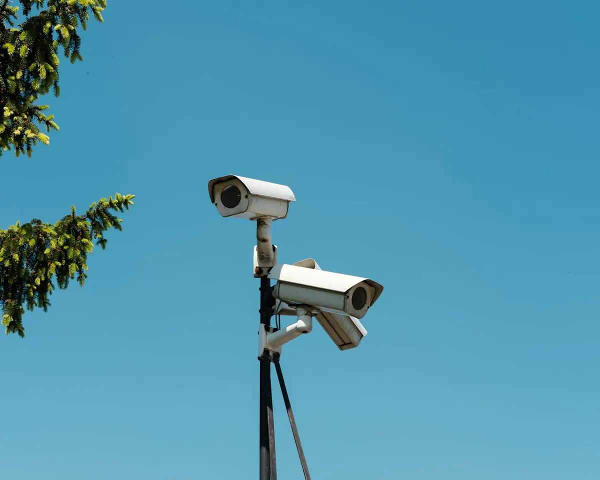 Two CCTV cameras mounted on a pole against a blue sky